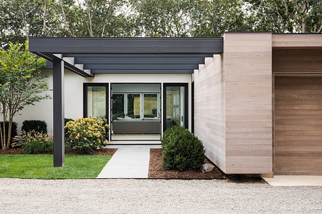 Modern, minimalist home with clean lines, neutral tones, and glass entryway surrounded by lush greenery.