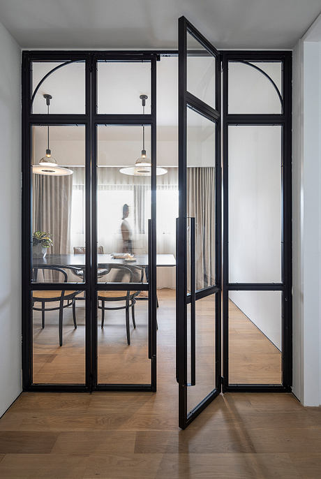 Sleek black metal frames enclosing glass doors and windows, leading to a cozy dining area.