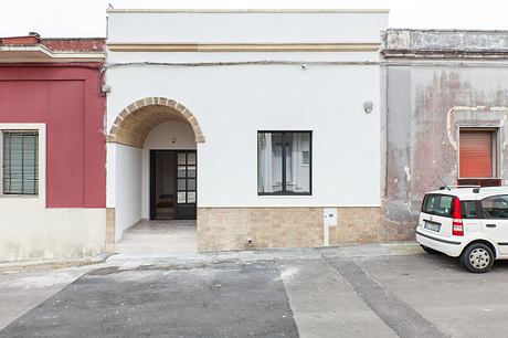 Arched entryway, white facade, brick detailing, and a parked car on the street.