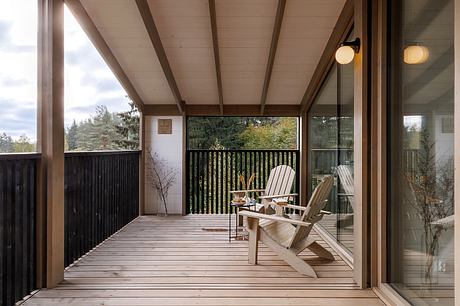 Cozy wooden deck with Adirondack chairs, glass walls, and treetop view.