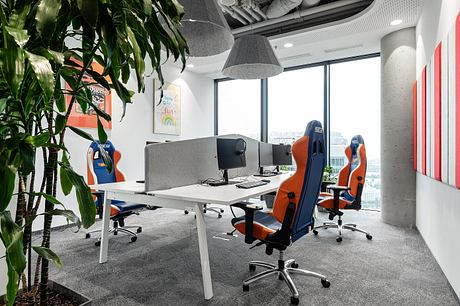 Modern open office space with sleek furniture, large windows, and lush plants.