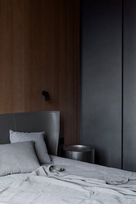 Minimalist bedroom with dark wood paneling, gray bedding, and circular side table.