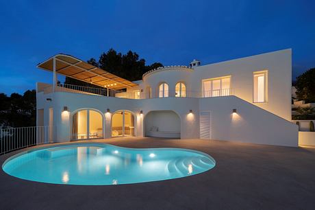 Elegant Mediterranean-style villa with arched windows, terrace, and illuminated pool.
