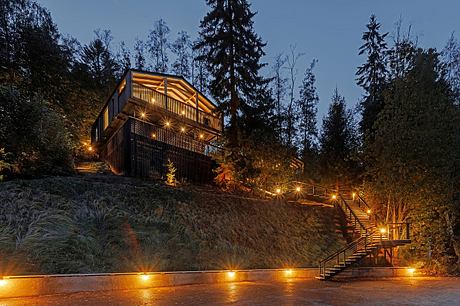 A cozy wooden cabin nestled in a forested landscape, lit by warm outdoor lighting creating a tranquil ambiance.