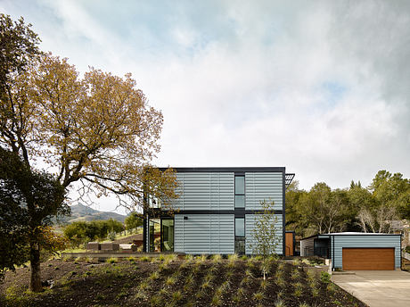 Modern, sleek home with large windows, wood accents, and a surrounding garden in a wooded setting.