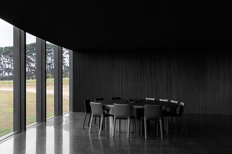 Modern architectural interior with dark, sleek furnishings and expansive windows overlooking lush greenery.
