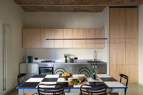 Rustic exposed brick ceiling, minimalist wooden cabinetry, and a checkered dining table.