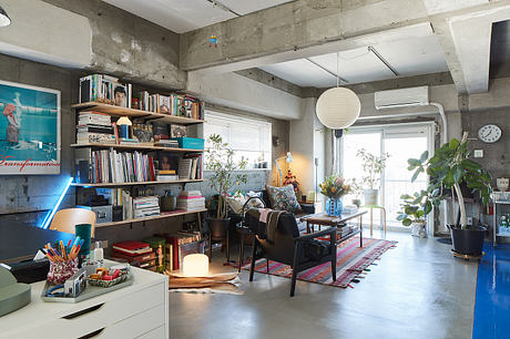 Spacious loft-style living space with concrete walls, bookshelves, and plants creating a cozy atmosphere.