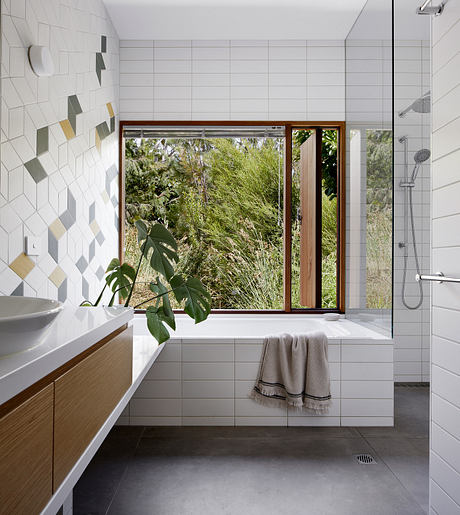 Sleek, modern bathroom with geometric tile patterns, large window framing lush outdoor view.