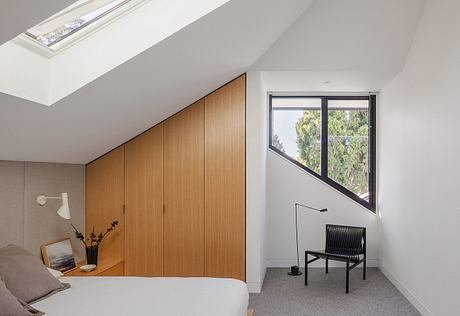 Minimalist bedroom with wooden built-in wardrobe, large window, and black accent chair.