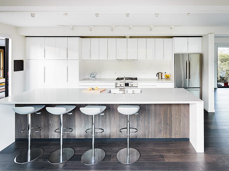 Sleek, modern kitchen with white cabinets, wood-paneled island, and chrome bar stools.