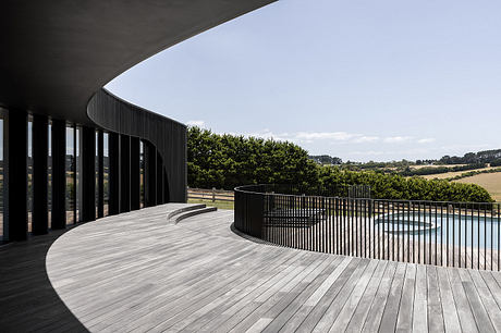 Curved, glass-walled structure with a wooden deck overlooking a pastoral landscape.