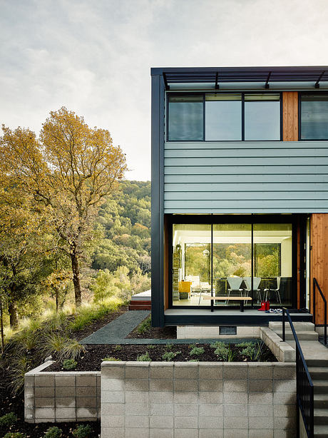 A modern architectural design with large windows overlooking a lush, forested landscape.