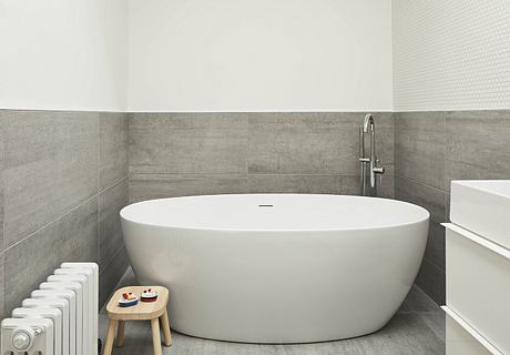 Modern bathroom with a large, oval-shaped bathtub, gray tiles, and a wooden stool.