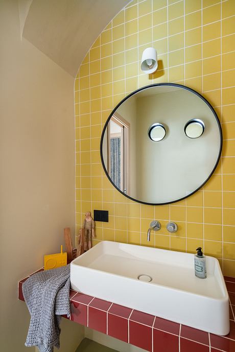 A modern bathroom with a curved arched wall, a round mirror, and colorful tiled walls.