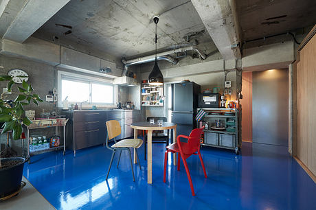 Industrial-style kitchen with concrete walls, exposed pipes, and a vibrant blue floor.
