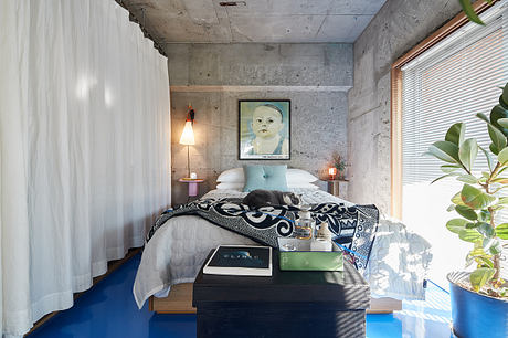 Cozy bedroom with concrete walls, wooden furniture, and modern artwork on display.