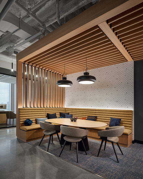 Contemporary office lounge with wood-paneled ceiling, cushioned seating, and pendant lights.