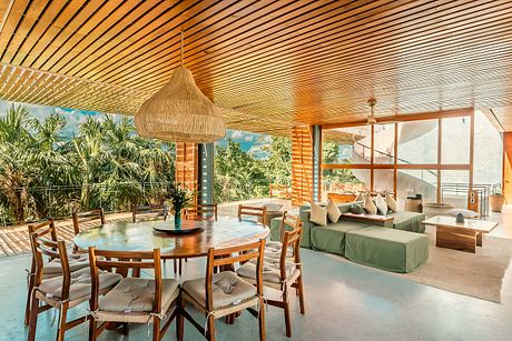 Spacious, open-concept living space with wooden beams, tropical foliage, and modern furnishings.