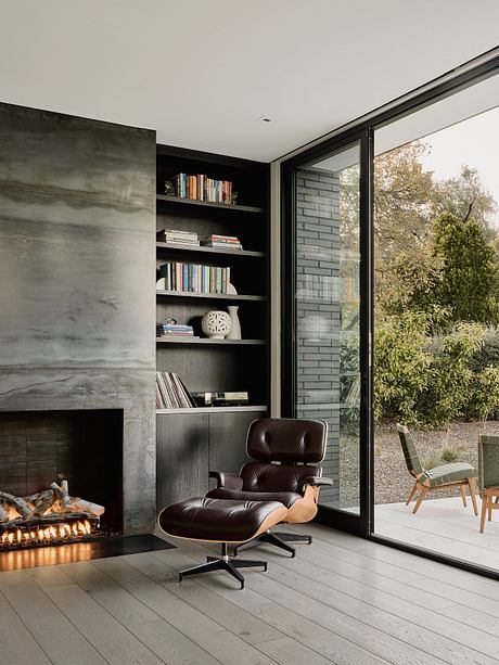 Modern living room with built-in shelves, leather armchair, and large window overlooking nature.