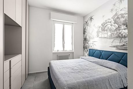 A cozy bedroom with a large window, a patterned gray bedding set, and a tropical mural wall.