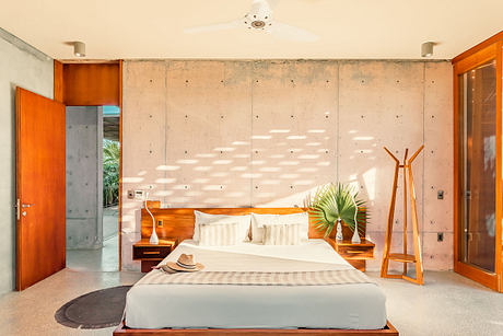 Modern, minimalist bedroom with concrete walls, warm wood furnishings, and tropical accents.
