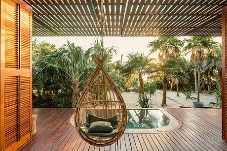Tropical outdoor retreat with hanging rattan chair and lush greenery surrounding a wooden deck.