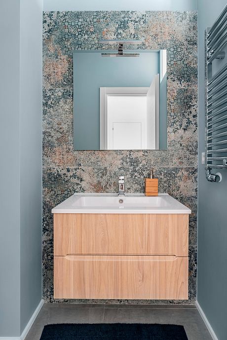 Minimalist bathroom design with wooden vanity, patterned tile wall, and sleek chrome faucet.