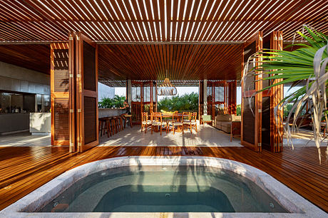Luxurious open-plan tropical villa with wooden slat ceiling, spa pool, and plush furnishings.