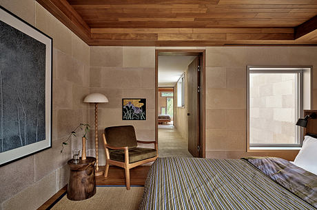 Warm, earthy-toned bedroom with wooden ceiling, stone walls, and mid-century armchair.