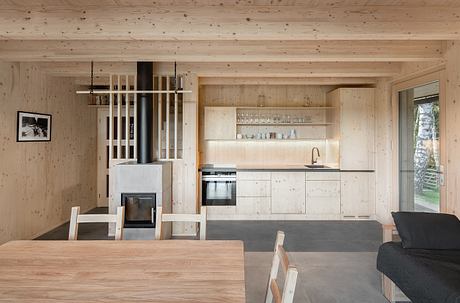 A cozy cabin interior with wooden walls, a wood-burning stove, and a modern, minimalist kitchen.