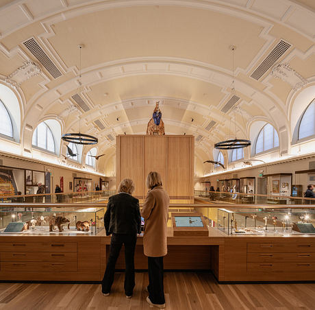 Ornate, vaulted ceiling with intricate architectural details; visitors browsing displays.