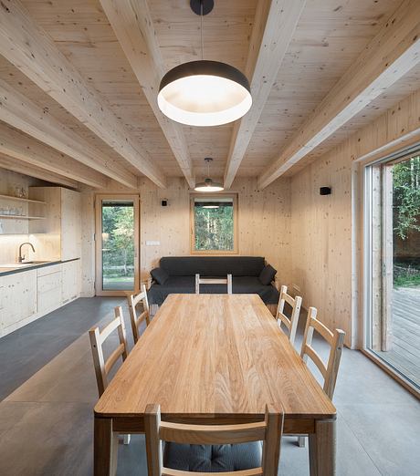 A cozy, rustic interior with a large wooden table, plush sofa, and natural light through windows.