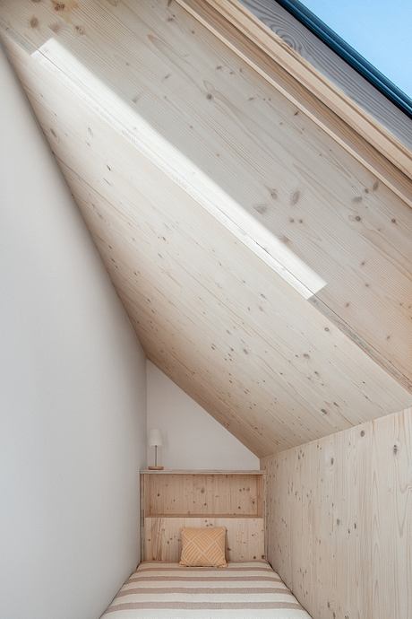 Cozy wooden alcove with angled ceiling, bed, and decorative pillow.