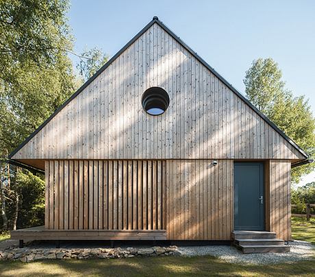 A wooden cabin-style home with a triangular gabled roof, vertical slat siding, and a central circular window.