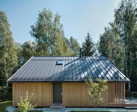 A wooden cabin with a sleek, dark-colored metal roof set against a forested backdrop.
