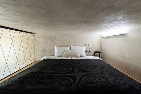 Minimalist bedroom interior with concrete walls, angular wood paneling, and a large black bedspread.