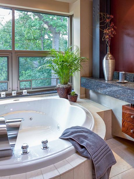 Luxurious bathroom with large window overlooking lush greenery, elegant granite countertop, and decorative vase.
