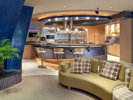 Modern kitchen with curved bar, chrome appliances, and plush sofa seating.