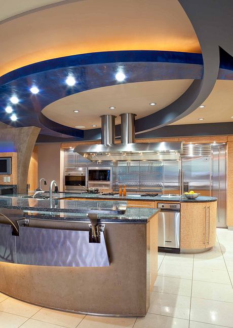 A modern kitchen with a curved, illuminated ceiling, stainless steel appliances, and granite countertops.