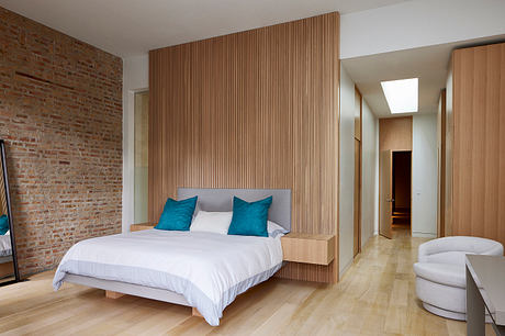 A modern bedroom with a wood-paneled accent wall, white bed, and turquoise accents.