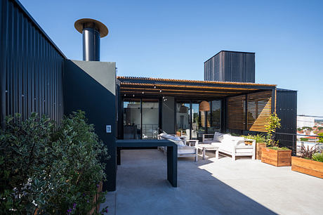 Modern outdoor patio with sleek black exterior, wooden pergola, and comfortable seating.