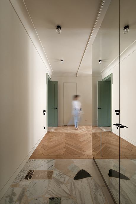 A minimalist hallway with herringbone wood flooring, marble tiles, and green doors.