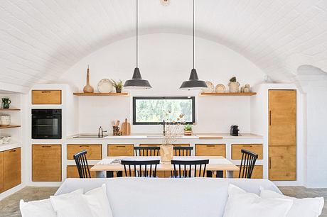 Cozy rustic kitchen with wooden cabinets, pendant lamps, and a dining table with black chairs.