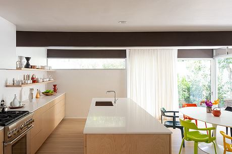 A modern kitchen with sleek cabinetry, open shelving, and large windows offering a view of the outdoors.