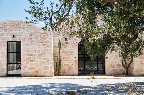 Stone walls, arched windows, and lush olive trees create a serene Mediterranean atmosphere.