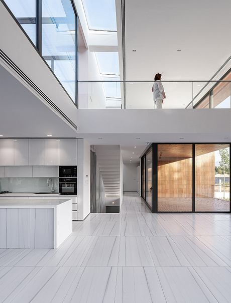 Spacious modern interior with sleek kitchen, glass walls, and a person visible in the distance.