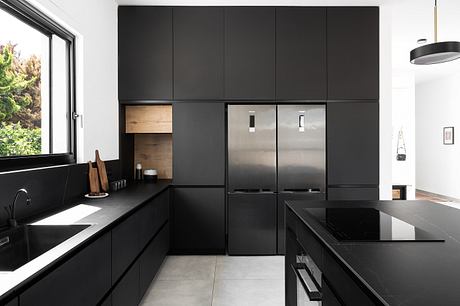 Modern, minimalist kitchen with sleek black cabinetry, stainless steel appliances, and a large window offering a natural view.