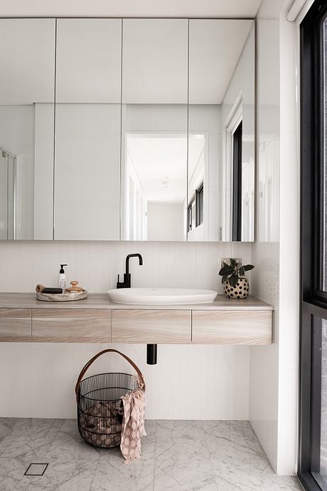 A modern, minimalist bathroom with a white vessel sink, wooden vanity, and patterned accessory.