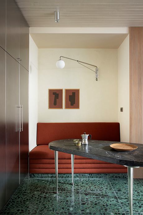 Sleek modern kitchen nook with red upholstered bench, marble table, and minimalist artwork.